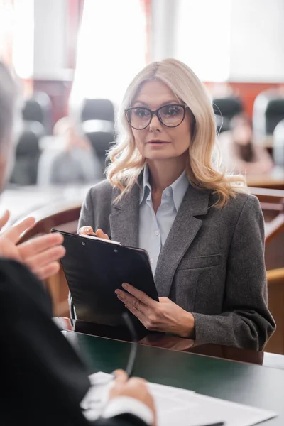 Juge floue pointant avec la main à l'avocat blonde tenant presse-papiers dans la salle d'audience — Photo de stock