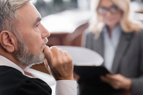 Selective focus of senior judge thinking near blurred attorney in courtroom — Stock Photo