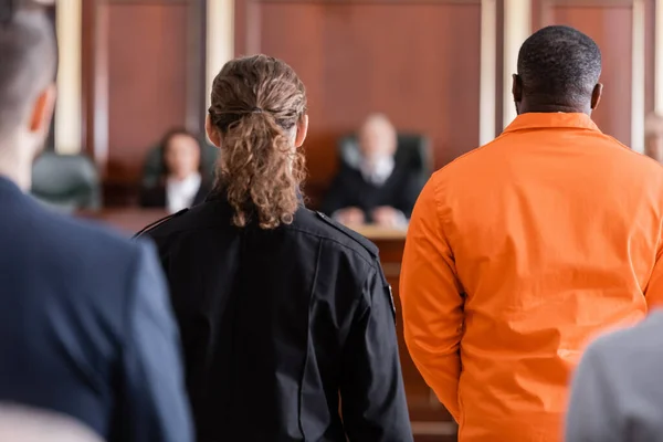 Back view of accused african american man near guard and blurred jurors in courtroom — Stock Photo