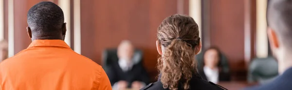 Back view of accused african american man, bailiff and juryman in courtroom, banner — Stock Photo