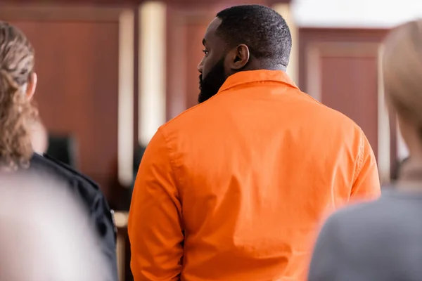 Back view of african american man in jail uniform near guard and blurred jurors in court — Stock Photo