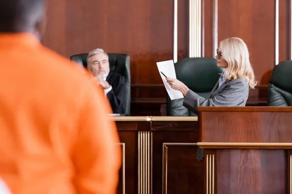 Avocat pointant vers procès près juge principal et accusé homme afro-américain sur le premier plan flou — Photo de stock