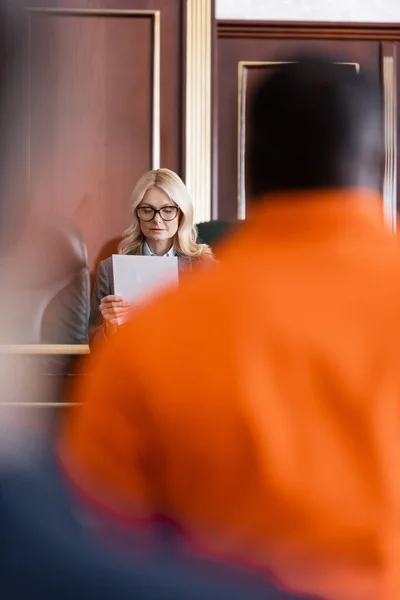 Advocate with document near accused african american man in courtroom on blurred foreground — Stock Photo