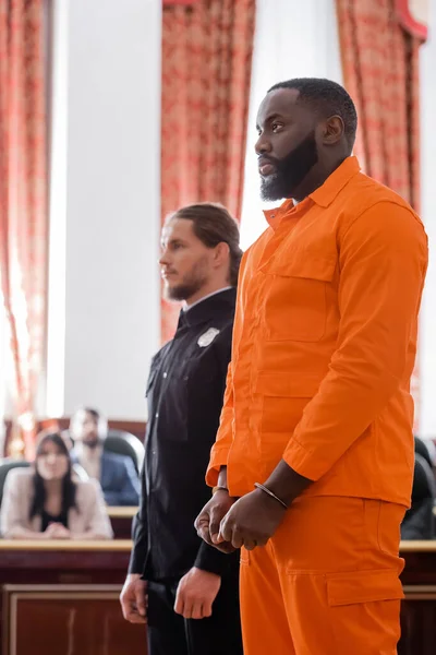 Handcuffed african american man standing near bailiff and blurred jurors in courtroom — Stock Photo