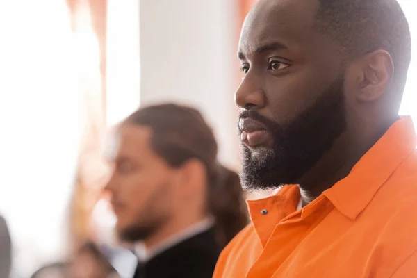 Selective focus of accused african man near blurred bailiff in courtroom — Stock Photo