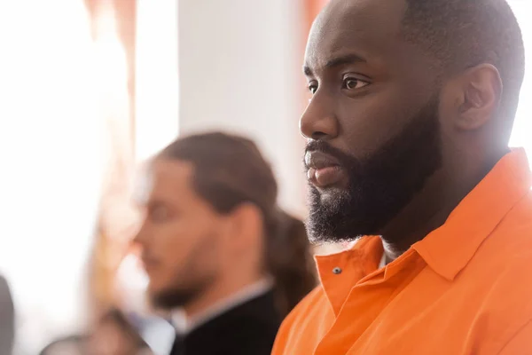 Enfoque selectivo del hombre africano acusado cerca del alguacil borroso en la sala del tribunal - foto de stock