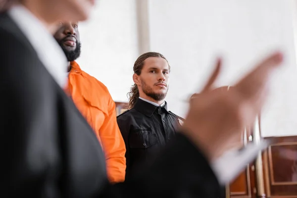 Bailiff looking at blurred prosecutor while standing near accused african amrican man in court — Stock Photo