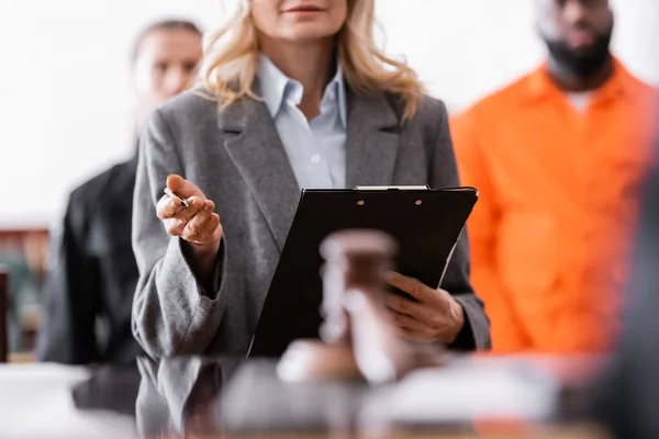 Advocate with clipboard standing near accused african american man and bailiff on blurred background — Stock Photo