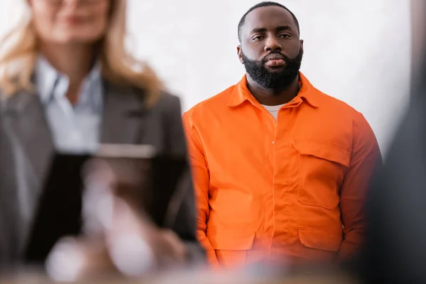 Africano americano hombre en naranja cárcel uniforme cerca advocate en borrosa primer plano - foto de stock