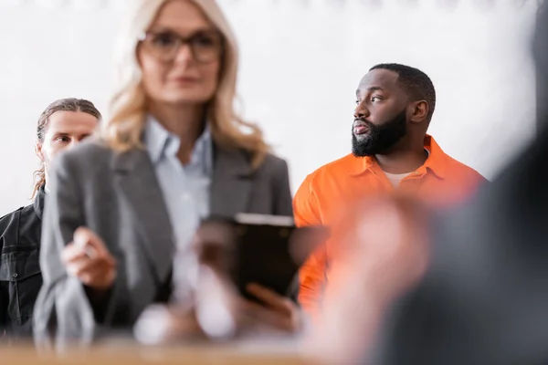 Accusé homme afro-américain regardant loin près huissier et avocat au premier plan flou — Photo de stock