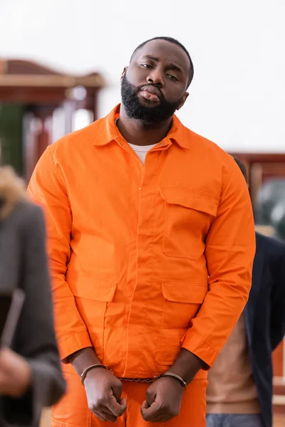 Menotté homme afro-américain en uniforme de prison orange dans la salle d'audience au premier plan flou — Stock Photo