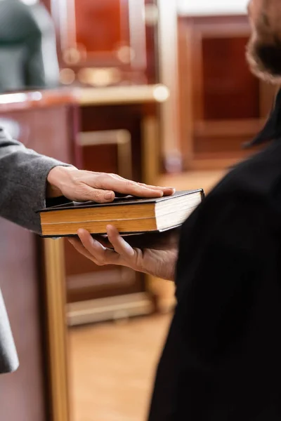 Partial view of woman swearing on bible near bailiff in court — Stock Photo