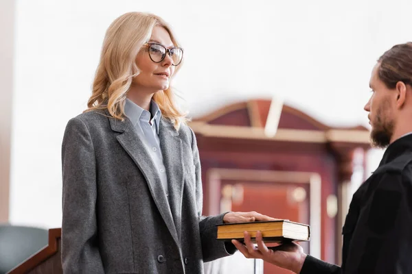 Middle aged woman in eyeglasses giving oath on bible in court — Stock Photo