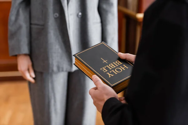 Teilansicht eines Gerichtsvollziehers mit heiliger Bibel in der Nähe einer Frau vor Gericht — Stockfoto