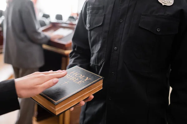 Visão parcial do oficial de justiça segurando bíblia perto de mulher dando juramento no tribunal — Fotografia de Stock