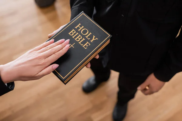 Vista recortada del testigo jurando sobre la Biblia cerca del alguacil en la corte - foto de stock