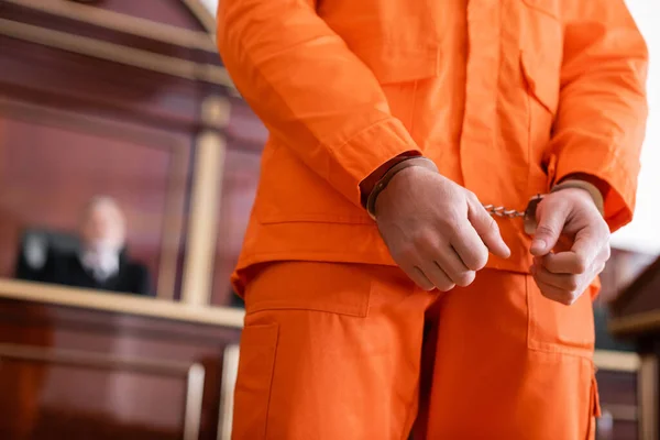 Partial view of handcuffed man in jail uniform in courtroom — Stock Photo