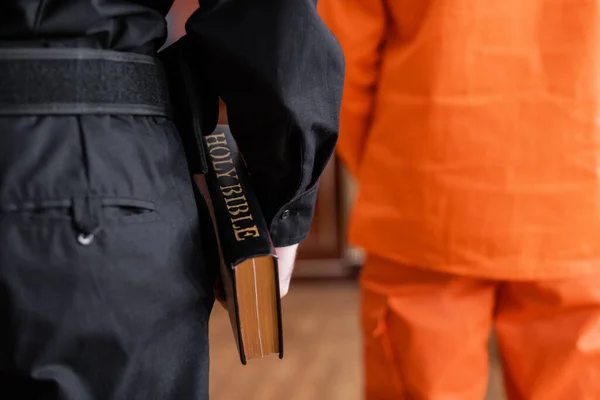 Back view of cropped bailiff holding bible while standing near accused man in court — Stock Photo