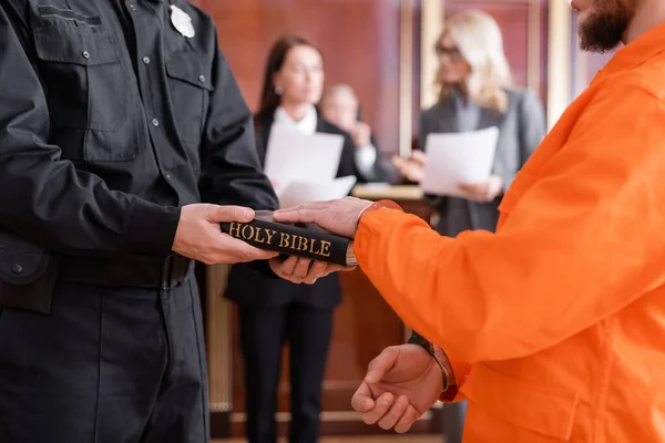 Oficial de justiça em uniforme segurando bíblia perto acusado homem dando juramento em tribunal — Fotografia de Stock