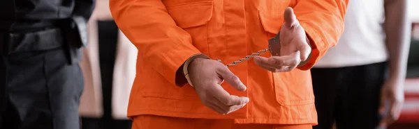 Обрізаний вид обвинуваченого у в'язничній формі та наручниках біля судових приставів та присяжних на розмитому тлі, банер — стокове фото