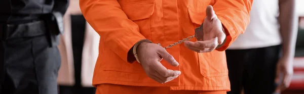 Vista ritagliata di uomo accusato in uniforme carcere e manette vicino ufficiale giudiziario e giurati su sfondo sfocato, banner — Foto stock