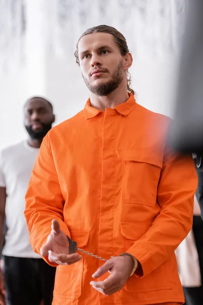 Hombre barbudo con esposas y uniforme de cárcel naranja gesticulando en la sala del tribunal - foto de stock