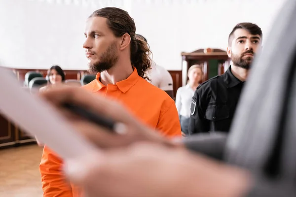 Accused man looking away near guard and blurred prosecutor in courtroom — Stock Photo