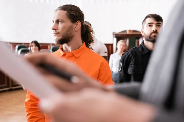 Acusado mirando hacia otro lado cerca de la guardia y difuminado fiscal en la sala del tribunal - foto de stock