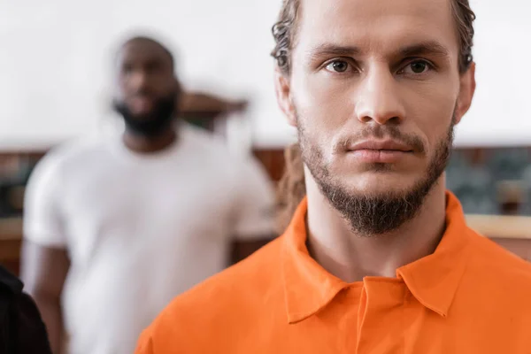 Bearded man in jail uniform looking at camera near blurred african american juryman — Stock Photo