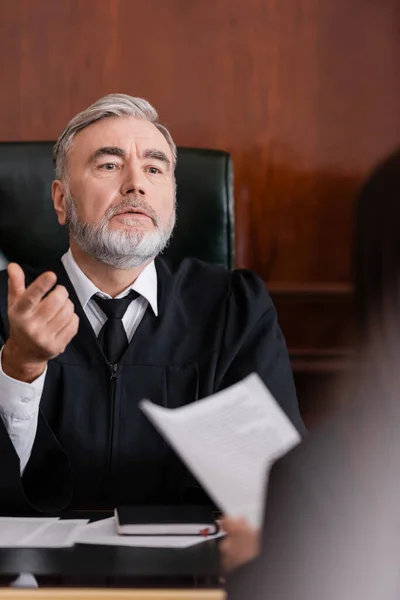 Senior judge pointing with finger while talking to blurred prosecutor in courtroom — Stock Photo