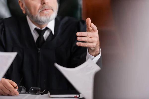 Cropped view of judge pointing with finger at prosecutor with lawsuit on blurred foreground — Stock Photo