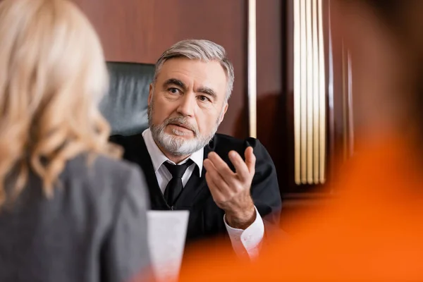 Juez mayor señalando con el dedo cerca de abogado borrosa en la corte - foto de stock