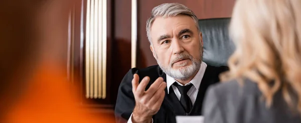 Senior judge pointing with finger while talking to blurred attorney in courtroom, banner — Stock Photo