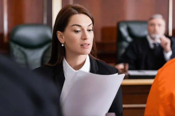 Brunette prosecutor reading lawsuit in court on blurred foreground — Stock Photo