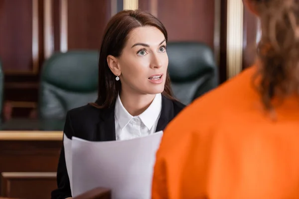 Prosecutor with lawsuit talking to accused man in courtroom on blurred foreground — Stock Photo