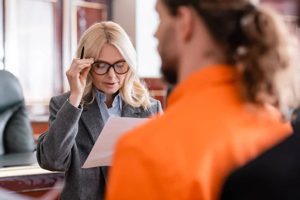 Anwalt justiert Brille, während er mit Papieren in der Nähe des Angeklagten im verschwommenen Vordergrund steht — Stockfoto