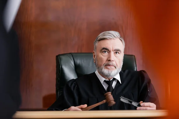 Juez serio sosteniendo martillo y anteojos en el tribunal en primer plano borrosa - foto de stock