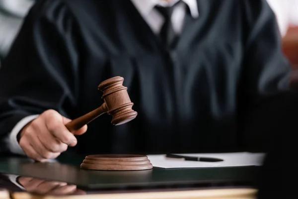 Partial view of blurred judge in robe holding gavel in court — Stock Photo