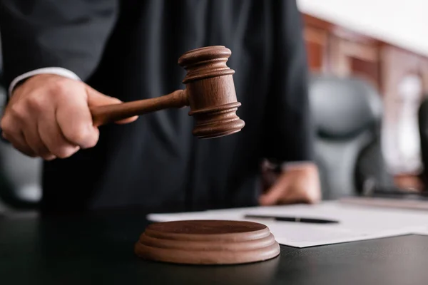 Partial view of blurred judge holding gavel during sentencing in court — Stock Photo