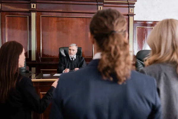 Fiscal hablando con el juez mayor cerca del hombre acusado y abogado en el tribunal - foto de stock