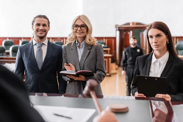 Smiling advocate pointing with hand near happy businessman and judge on blurred foreground — Stock Photo