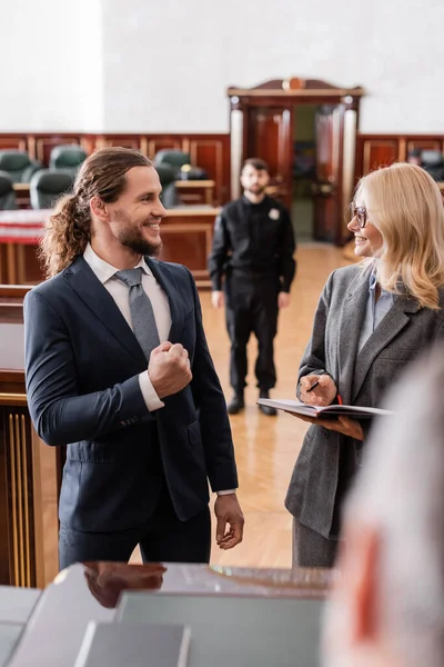 Justified businessman showing success gesture near smiling advocate and blurred judge in court — Stock Photo