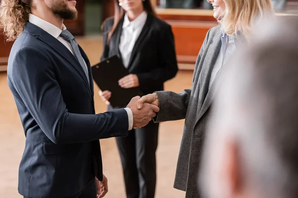 Partial view of justified businessman shaking hands with smiling advocate in court — Stock Photo