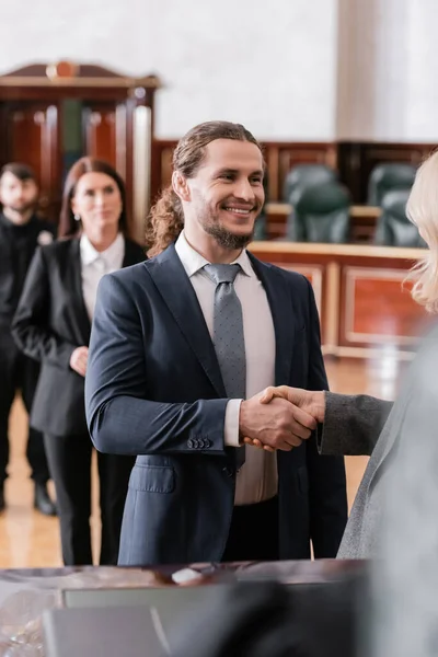 Cheerful businessman shaking hands with blurred attorney in courtroom — Stock Photo