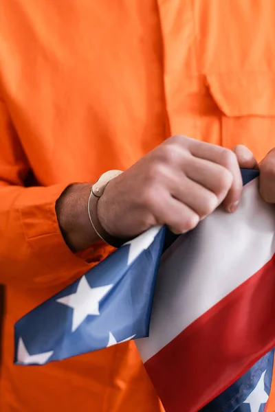 Vista recortada del hombre en uniforme de la cárcel y esposas rasgando la bandera americana, concepto de justicia - foto de stock