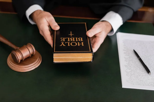 Частичный взгляд судьи, держащего библию возле молотка и судебный иск в законе — стоковое фото