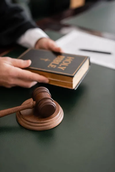 Partial view of blurred judge holding bible near gavel in court — Stock Photo