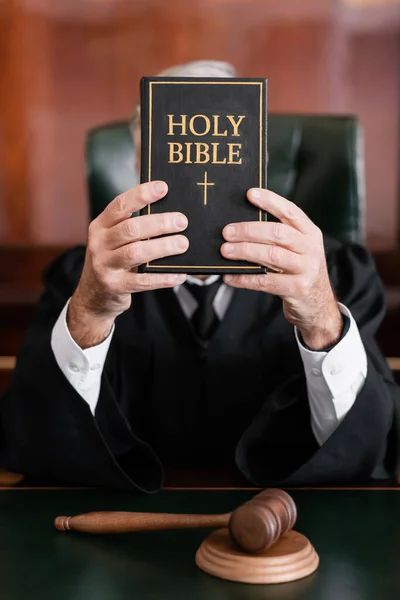 Священная Библия в руках старшего судьи в суде на размытом фоне — стоковое фото