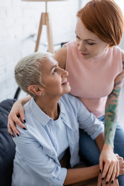 Tätowierte lesbische Frau schaut glückliche Freundin zu Hause an — Stockfoto