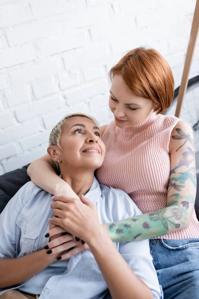 Tattooed woman hugging happy lesbian girlfriend while looking at each other at home — Stock Photo